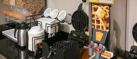 Un coin dédié aux gaufres, avec un appareil à gaufres, des assiettes et une machine à café.