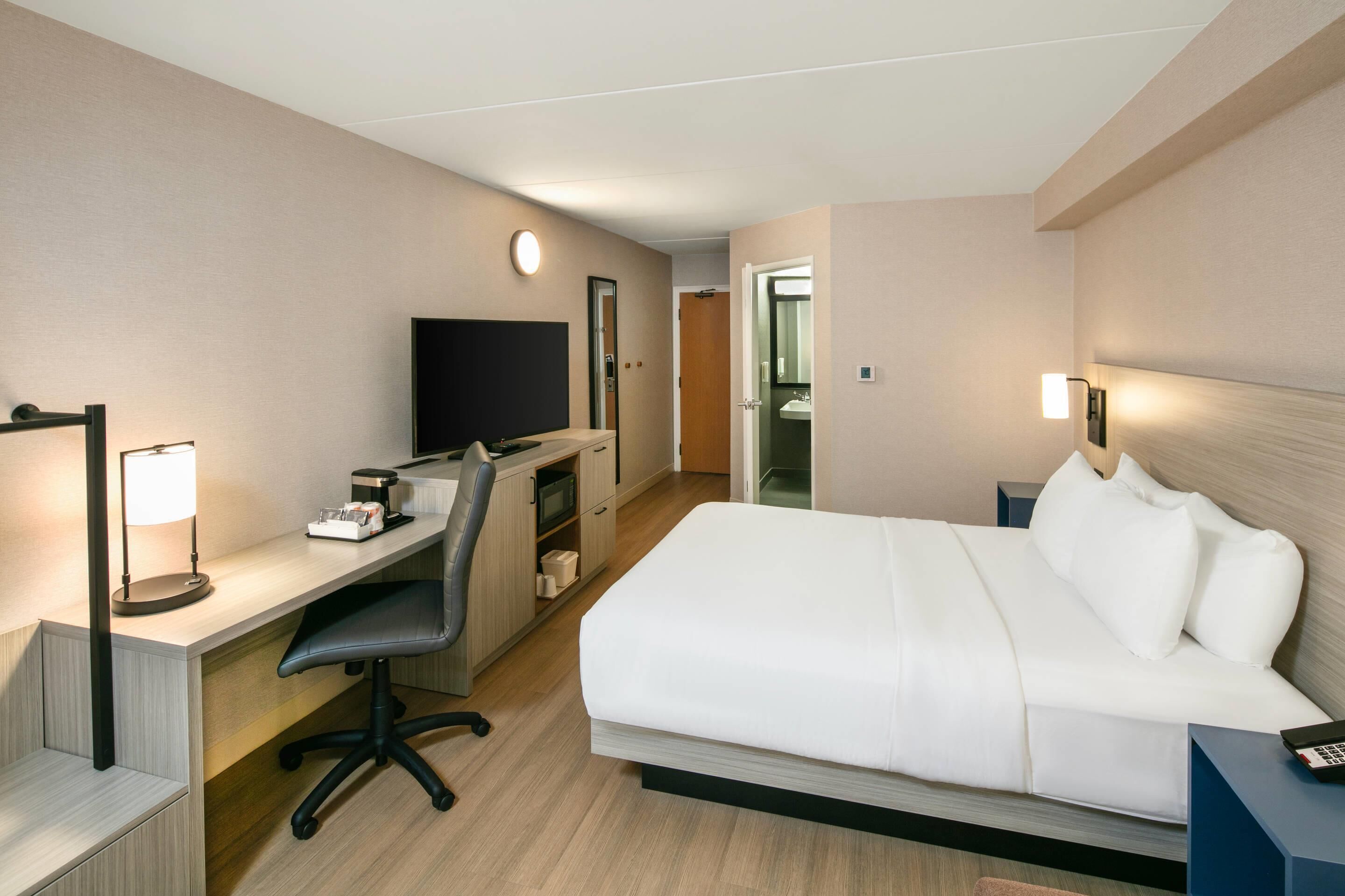 A hotel room with a bed, desk, chair, TV, and a bathroom visible through an open door.