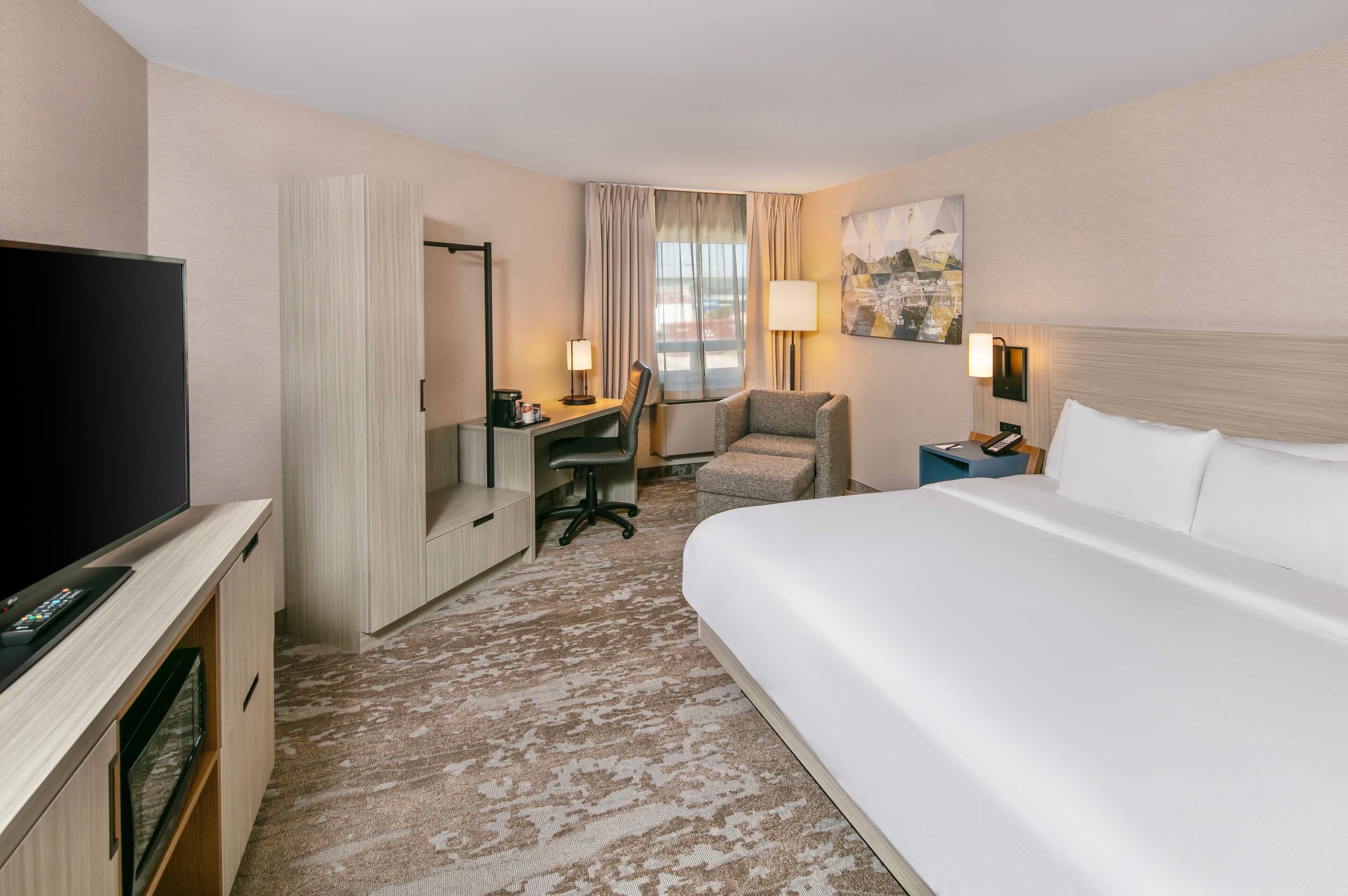 A hotel room with a bed, a desk, a chair, a television, and a painting on the wall.