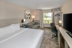 A hotel room with a bed, a desk, a chair, a TV, a painting, and a window with curtains. - Comfort Inn (Yarmouth)