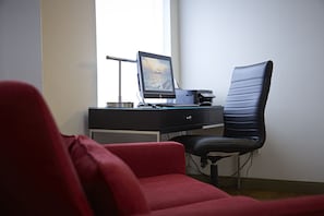 A workspace with a desk, computer, chair, and a red sofa.
