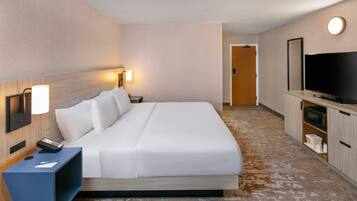 Een hotelkamer met een bed, nachtkastje, lamp, televisie en een klein keukenhoekje.