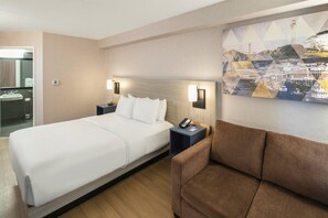 Ein Hotelzimmer mit einem großen Bett, einem Nachttisch mit Telefon, einem braunen Sessel und einer Wandleuchte.