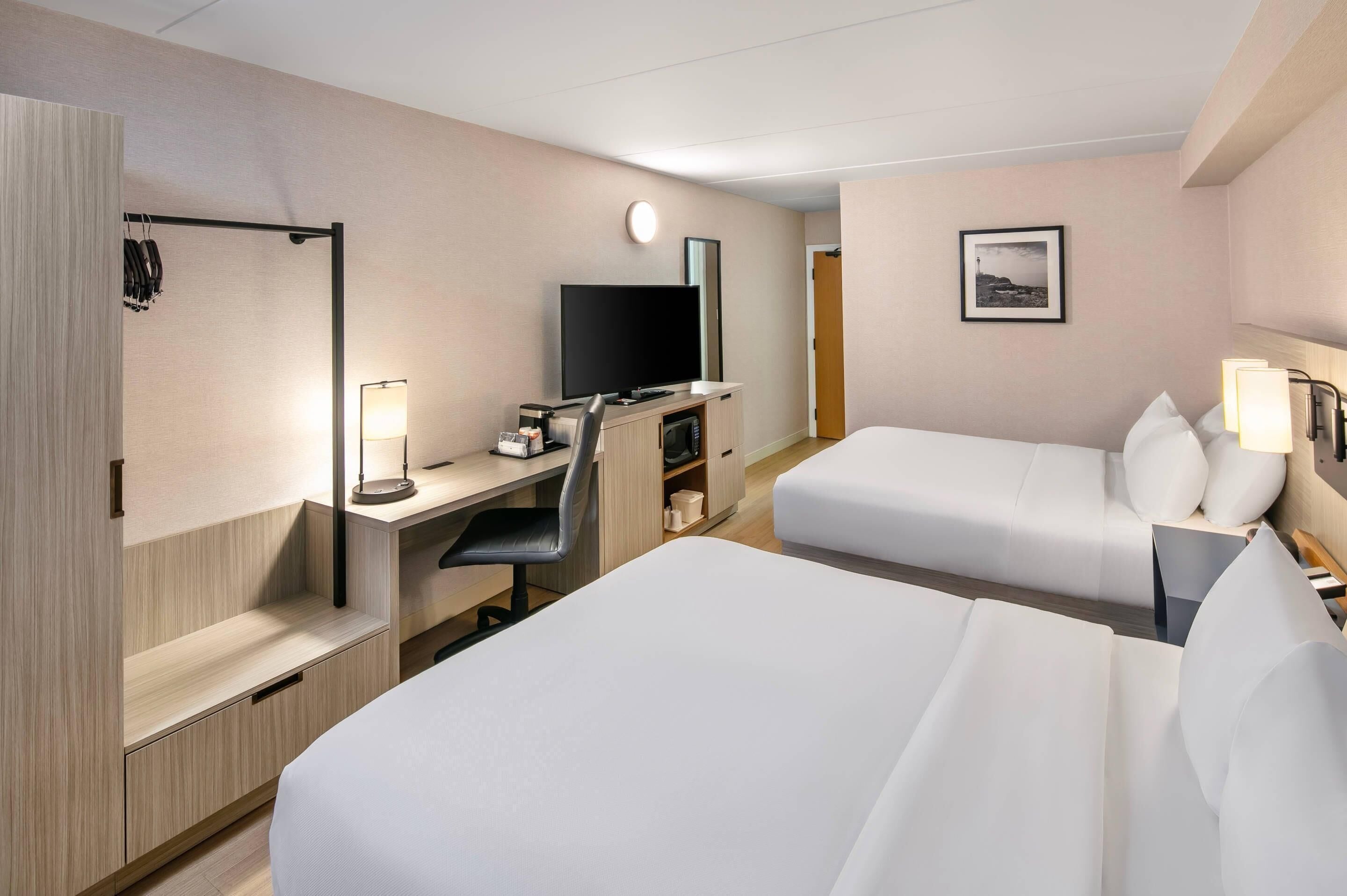 Une chambre d’hôtel avec deux lits, un bureau avec un ordinateur, une télévision et une table de chevet avec des lampes.