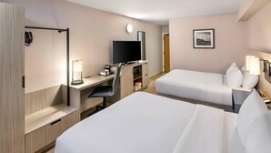 A hotel room with two beds, a desk with a computer, a TV, and a bedside table with lamps.