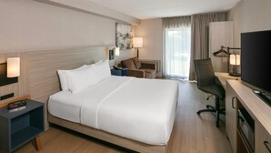 A hotel room with a bed, bedside table, lamp, chair, desk with a TV, and a window with curtains. - Comfort Inn (Yarmouth)