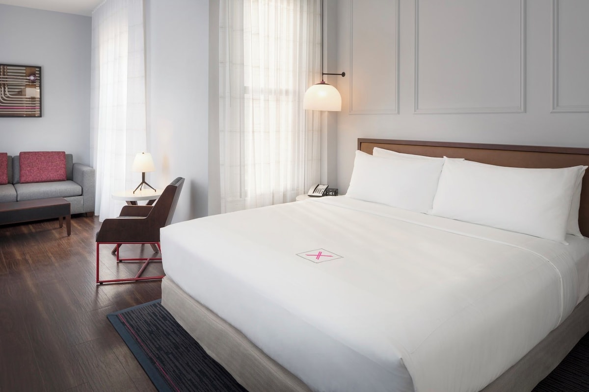 A hotel room with a large bed, a desk, a chair, and a sofa.