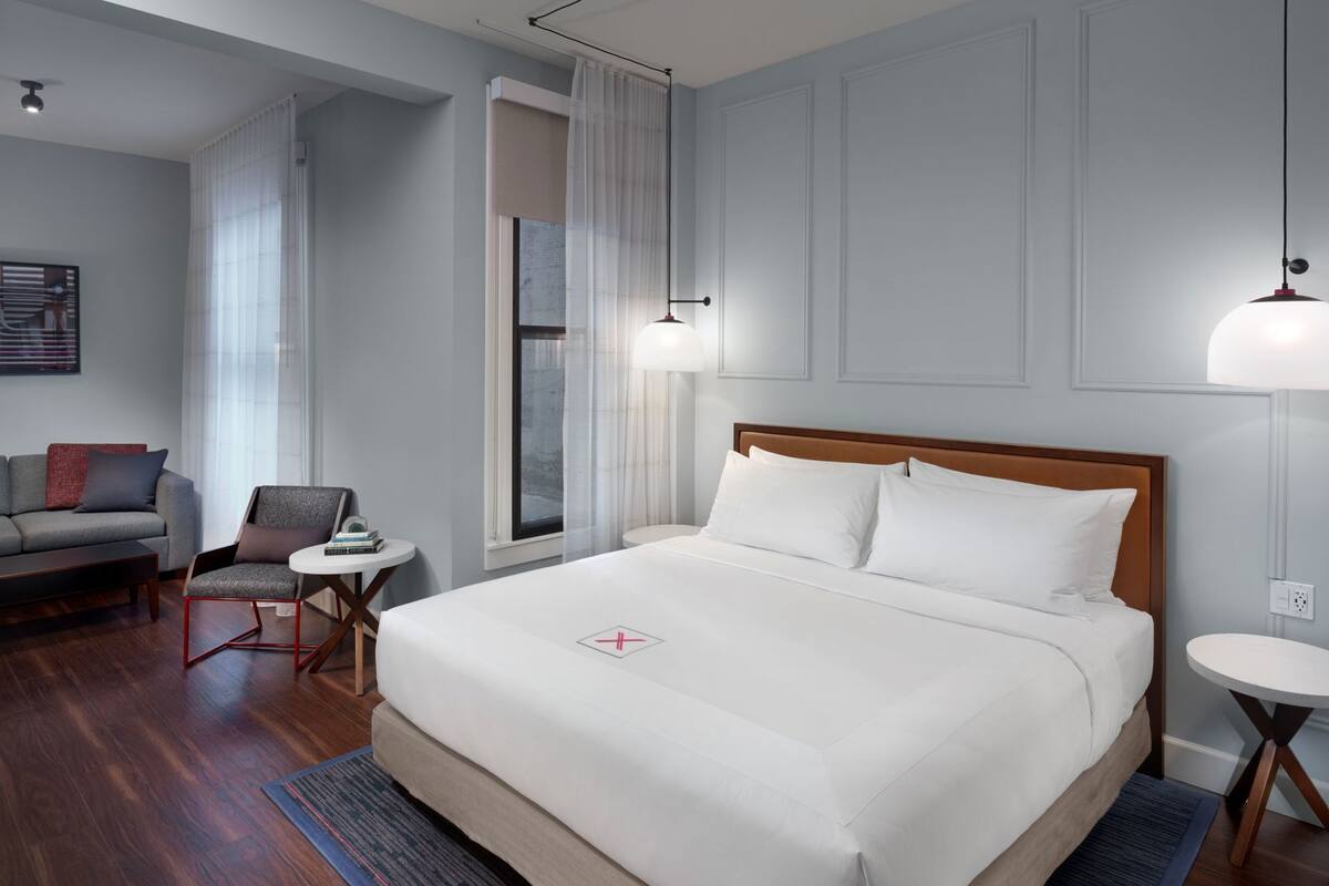 Una habitación de hotel con cama, sofá, sillón, mesita y lámpara.