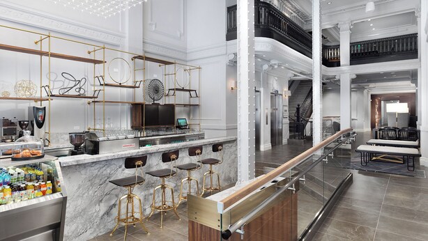 A modern bar area with a marble countertop, gold bar stools, and a glass enclosure with beverages.