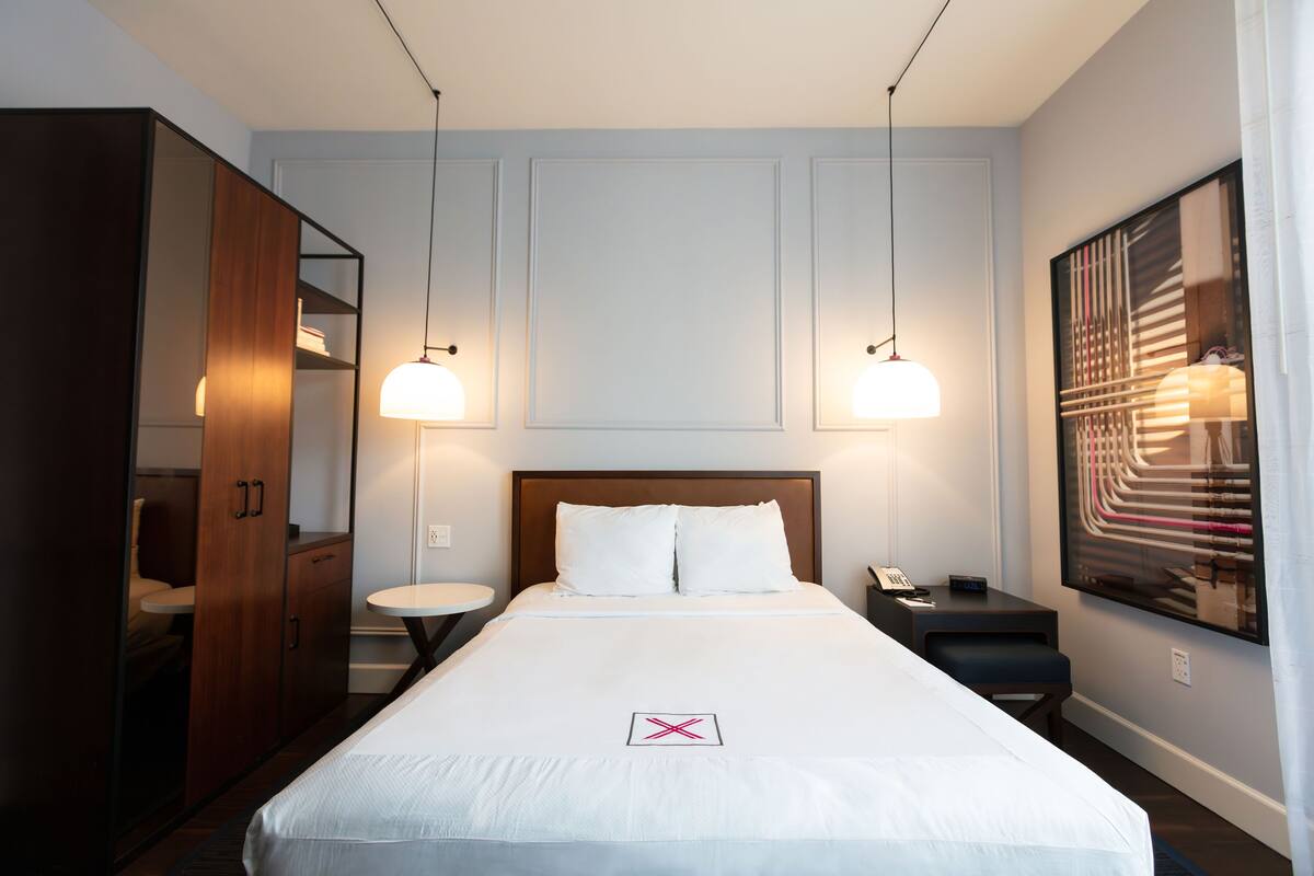 Una habitación de hotel con una cama grande, dos mesitas de noche, un escritorio, una silla, un armario y un cuadro en la pared.