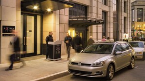 A hotel entrance with a prominent sign, a covered entrance, and a car parked in front.