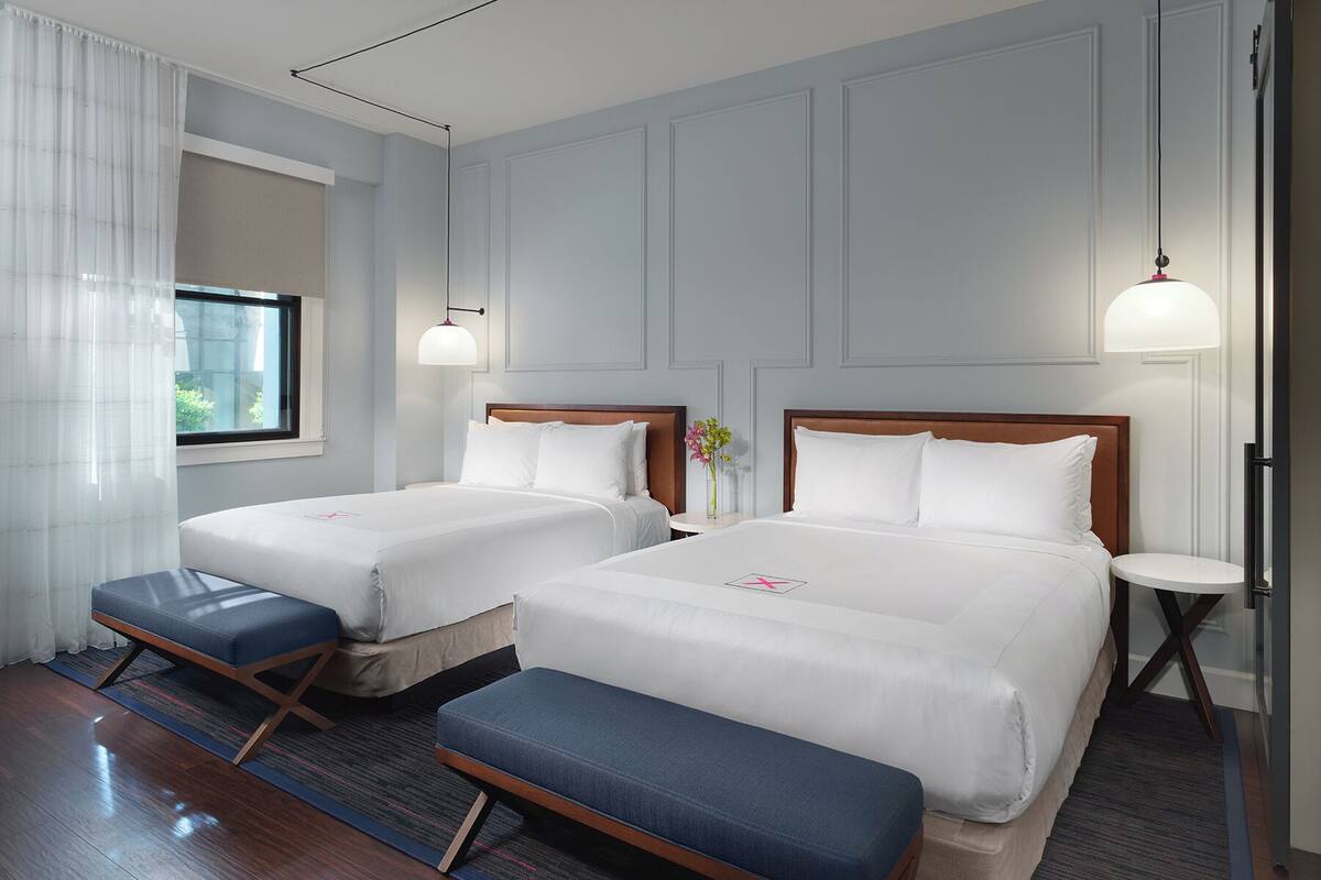 Una habitación de hotel con dos camas, un banco, una mesita y una ventana con cortinas.