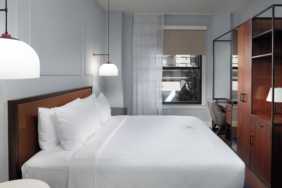 Habitación de hotel con una cama grande, un escritorio, un armario y una ventana con cortinas.