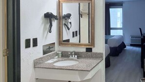 A bathroom with a granite countertop sink, a mirror with a gold frame, and a hairdryer mounted on the wall. - Rodeway Inn Enid South (Enid)