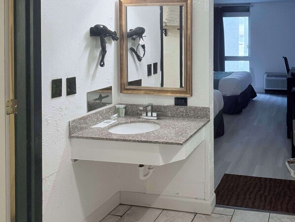 A bathroom with a granite countertop sink, a mirror with a gold frame, and a hairdryer mounted on the wall. - Rodeway Inn Enid South (Enid)