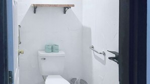 A small, compact bathroom with a toilet, a trash bin, and a shelf above the toilet holding toilet paper. - Rodeway Inn Enid South (Enid)