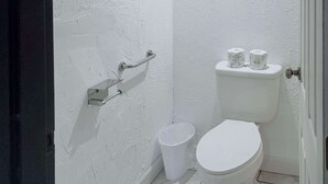 A small, clean bathroom with a white toilet, a handrail, and a trash bin.