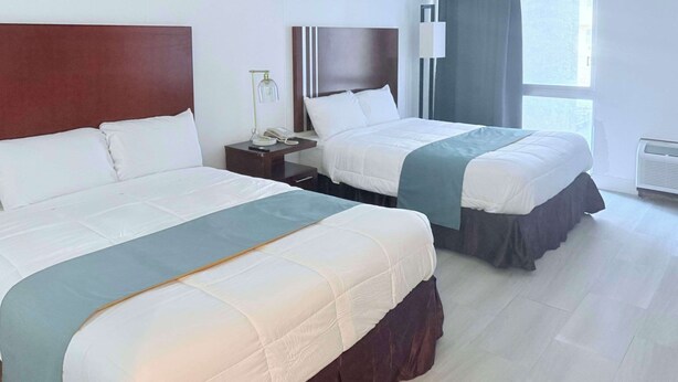 A hotel room with two beds, a nightstand with a phone and lamp, a window with curtains, and a radiator. - Rodeway Inn Enid South (Enid)