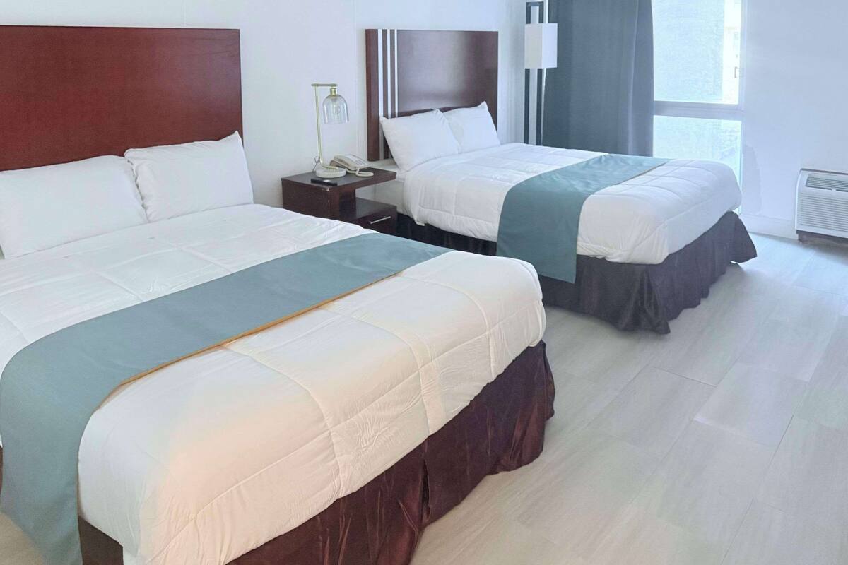 Ein Hotelzimmer mit zwei Betten, einem Nachttisch mit Telefon und Lampe, einem Fenster mit Vorhängen und einem Heizkörper.