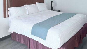 A neatly made bed with a white and blue bedspread, a wooden headboard, and a dark nightstand with a lamp. - Rodeway Inn Enid South (Enid)