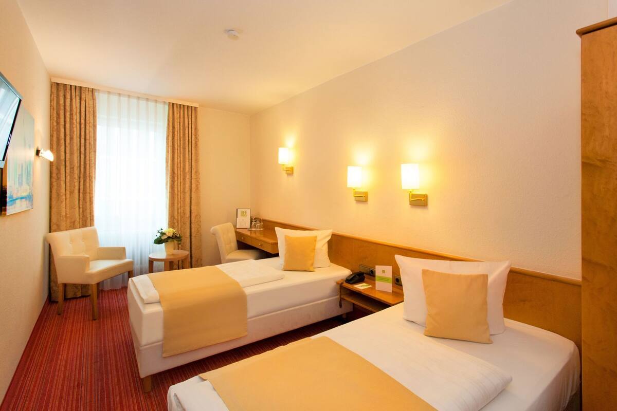 A hotel room with two beds, a desk, a chair, and a window with curtains.