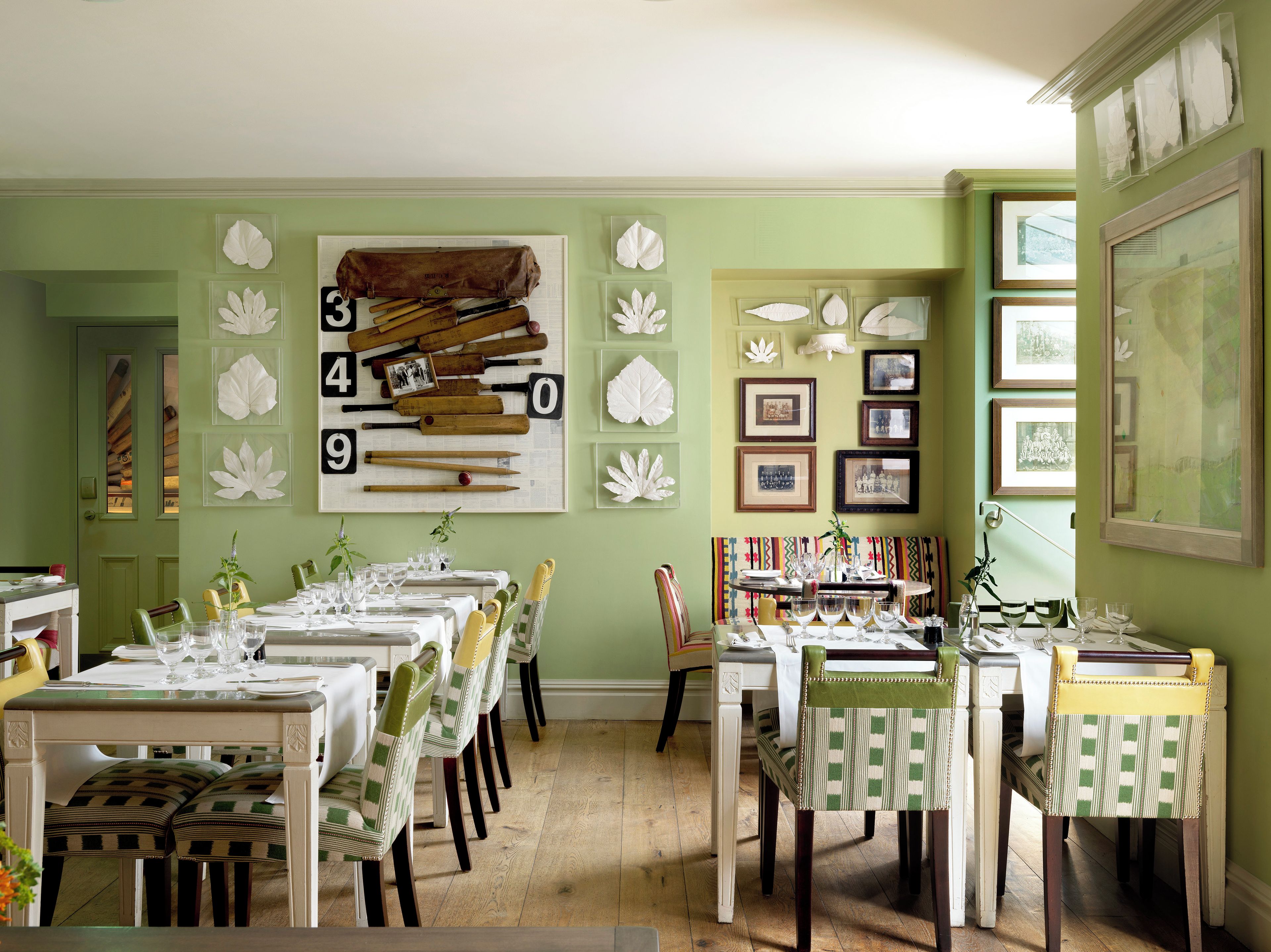 Un comedor con varias mesas dispuestas para comidas, sillas con tapicería estampada y una pared decorada con cuadros y un letrero con un número grande.