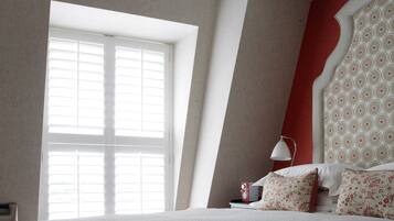 A bedroom with a large window, a bed with white bedding, a red accent wall, and a patterned headboard.
