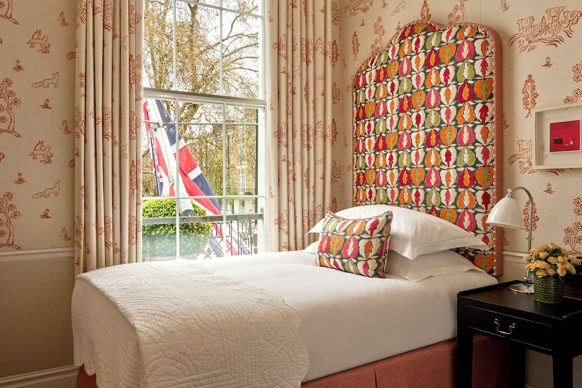 A bedroom with a bed, a nightstand, a lamp, and a window with curtains.
