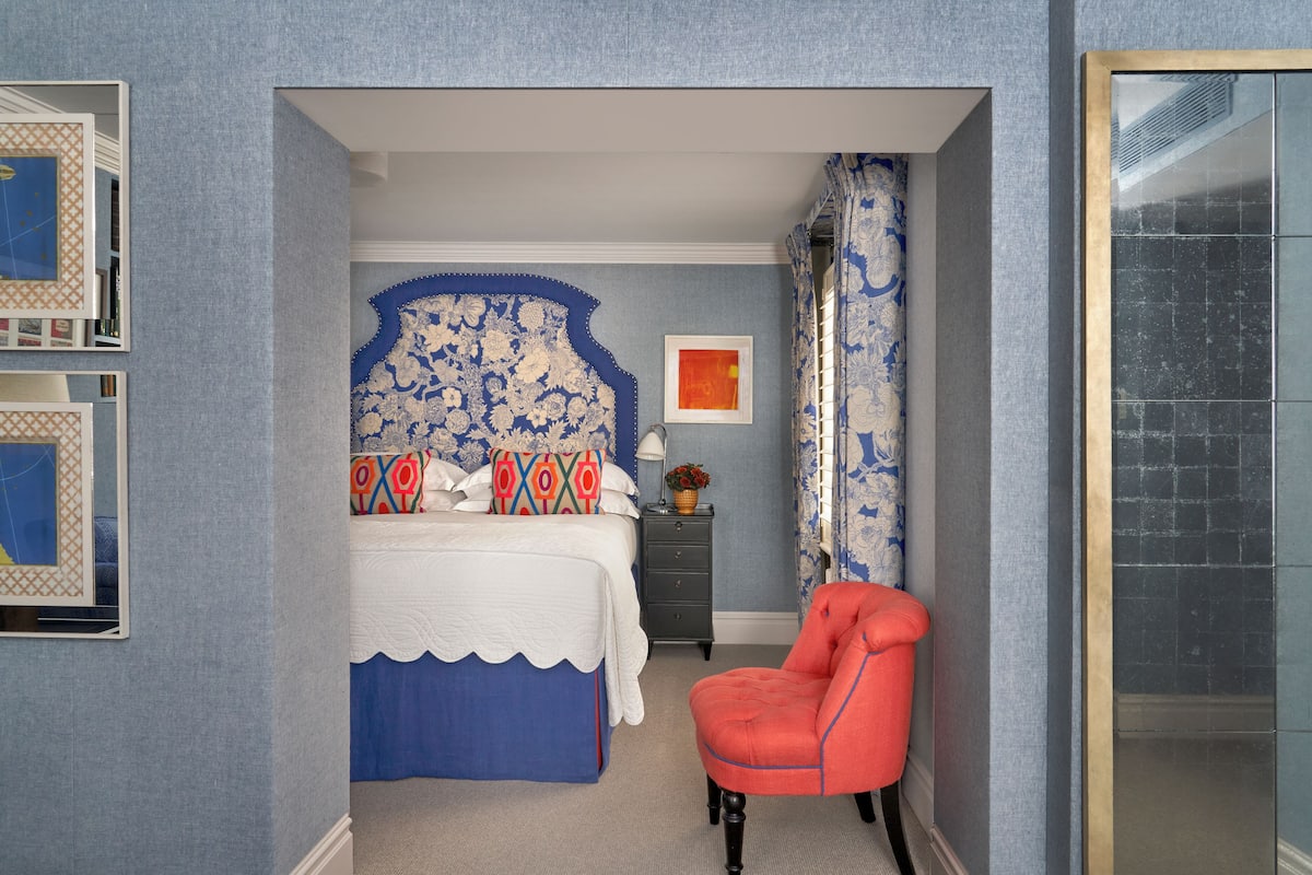 A bedroom with a bed, a chair, a nightstand, and a framed picture on the wall.