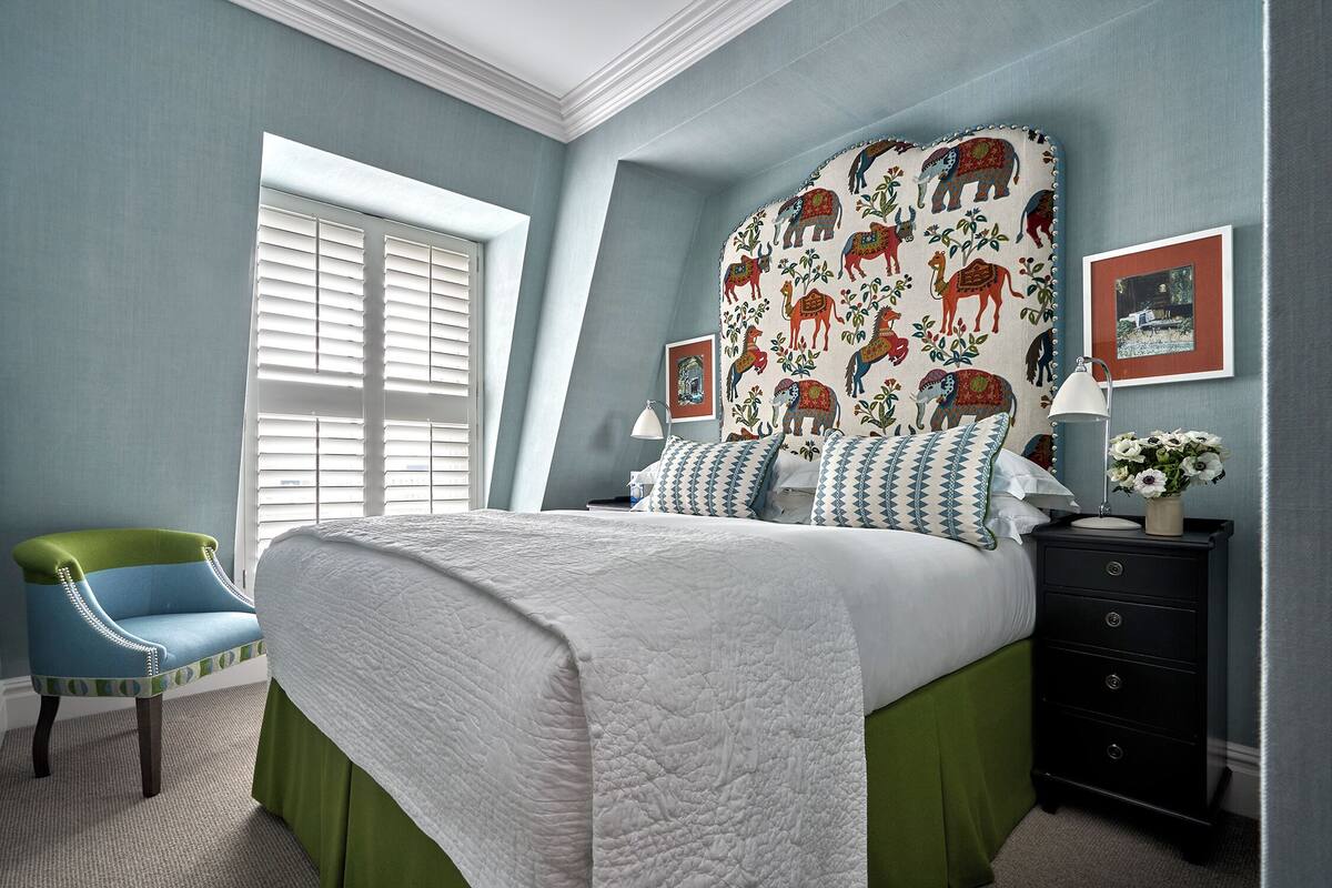 A bedroom with a bed, a chair, a dresser, and a window with blinds.