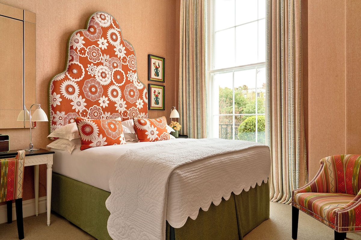 A bedroom with a large bed, a nightstand, a chair, and a window with curtains.
