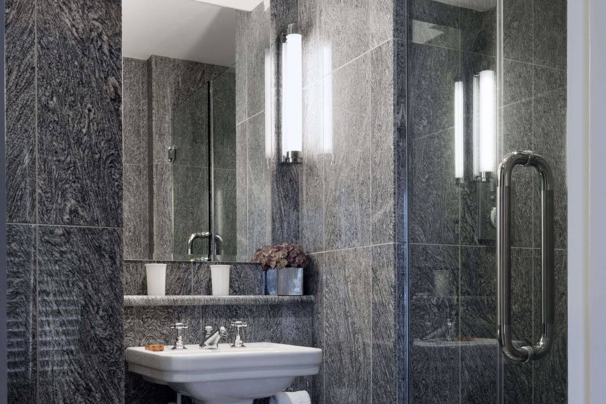 A modern bathroom with a pedestal sink, a glass shower enclosure, and marble walls.
