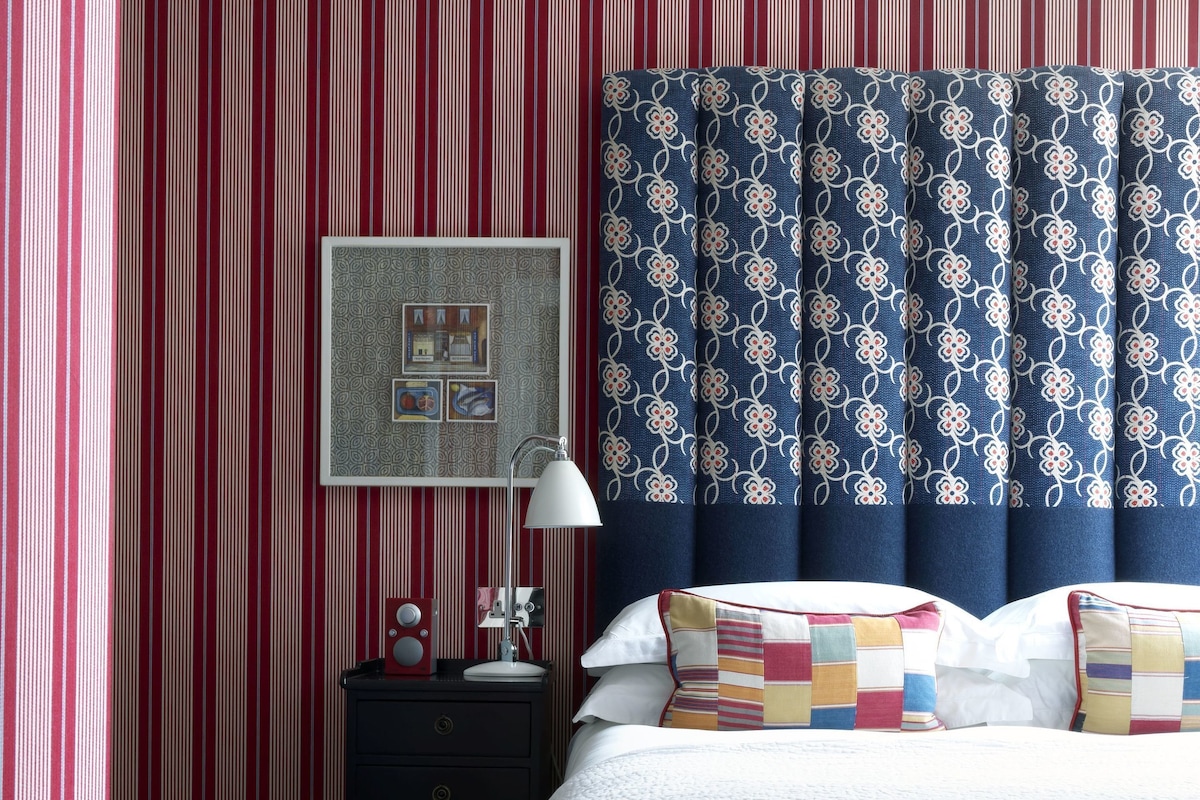 A neatly made bed with a white quilt, a nightstand with a lamp, a framed picture, and a striped wall.