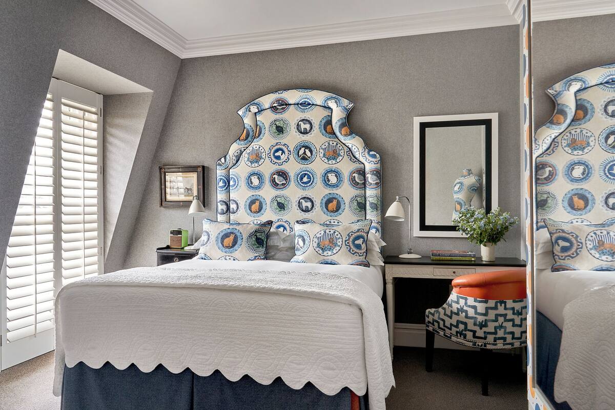 A bedroom with a bed, a desk, a chair, and a mirror.