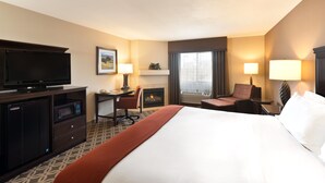 A hotel room with a large bed, a flat-screen TV, a desk with a chair, a fireplace, and a window with curtains. - Holiday Inn Express Show Low by IHG (Show Low)