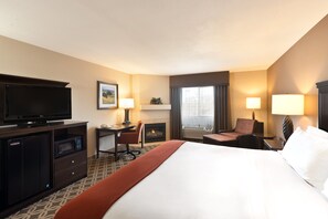A hotel room with a large bed, a flat-screen TV, a desk with a chair, a fireplace, and a window with curtains. - Holiday Inn Express Show Low by IHG (Show Low)