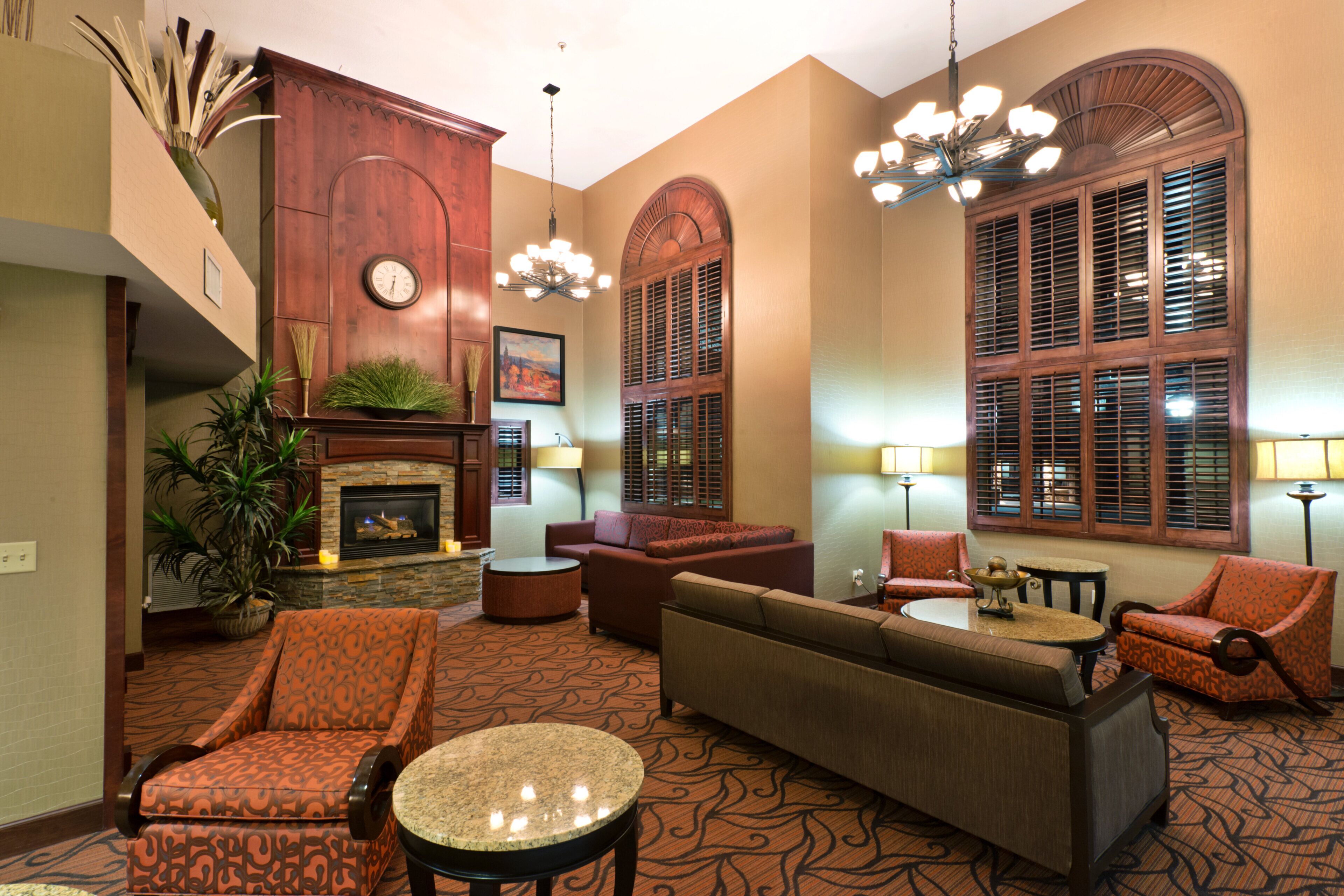 A hotel lobby with a fireplace, seating area, and large windows with shutters.