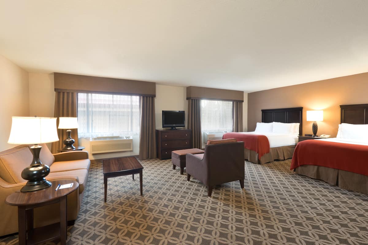 A hotel room with a sofa, two single beds, a TV, a desk, and a patterned carpet.