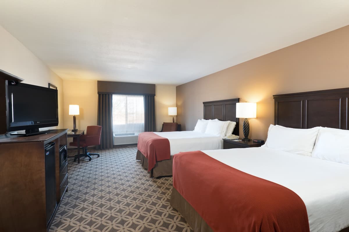 A hotel room with two beds, a desk with a television, and a window with curtains.