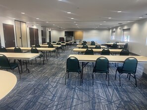 A conference room with multiple tables and chairs, carpeted floor, and a large screen at the front. - Holiday Inn Express Show Low by IHG (Show Low)