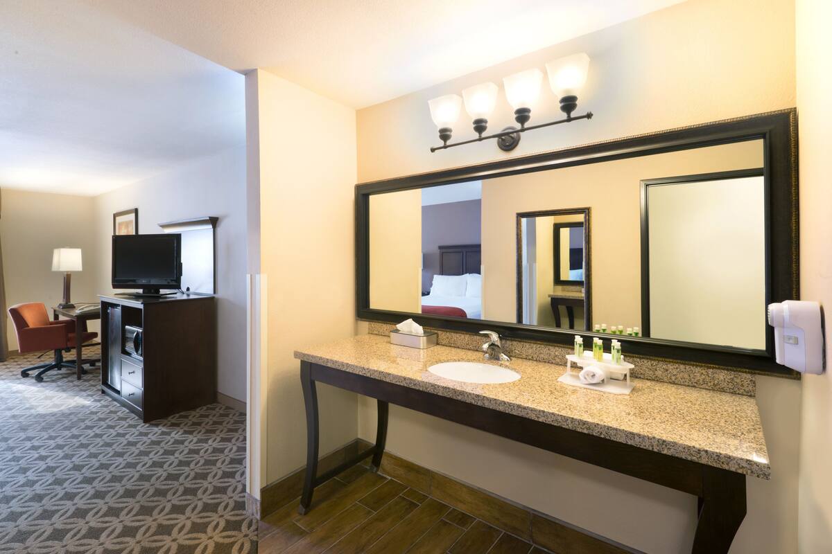 A hotel bathroom with a sink, mirror, and toiletries.