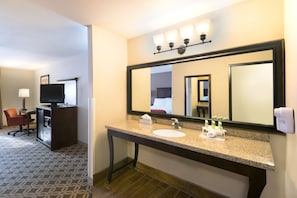 A hotel bathroom with a sink, mirror, and toiletries.