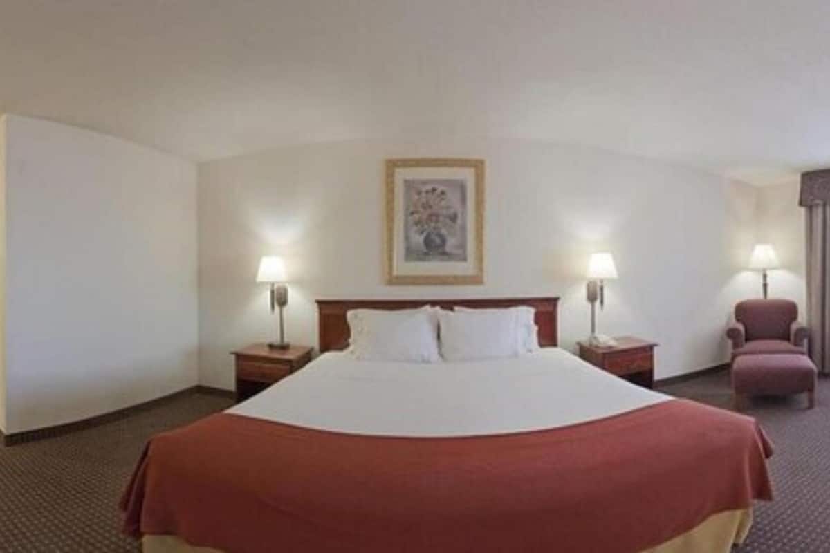 A hotel room with a large bed, two bedside tables with lamps, a chair, and a window with curtains.