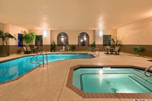 A pool area with two pools, lounge chairs, and potted plants.