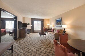 A hotel room with a patterned carpet, a sofa, a dining table, a TV, and a window with curtains. - Holiday Inn Express Show Low by IHG (Show Low)