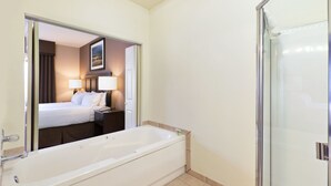A hotel bathroom with a large bathtub, a shower area, and a bed visible through a mirror. - Holiday Inn Express Show Low by IHG (Show Low)
