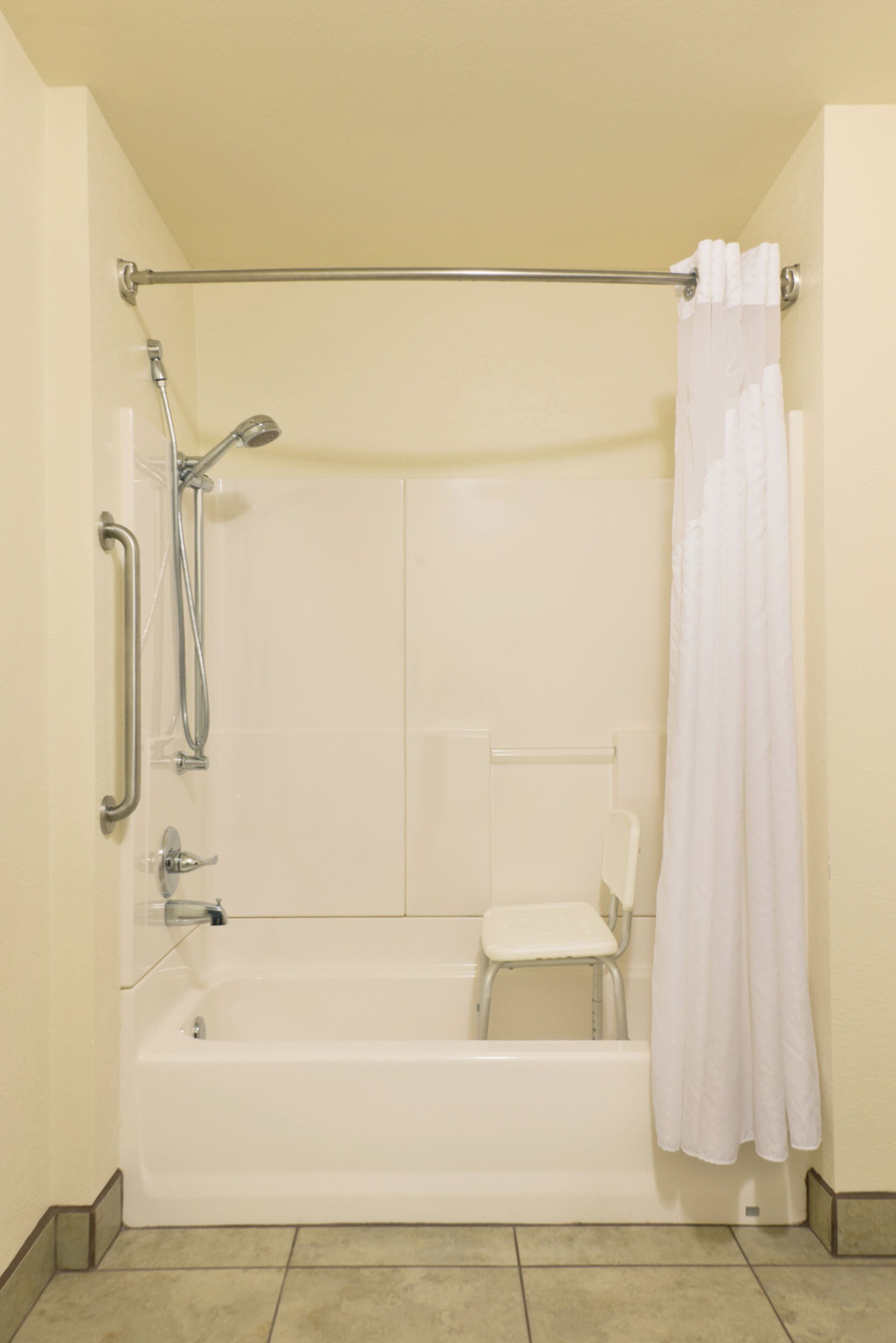 A standard bathtub with a showerhead and grab bars, a white chair, and a shower curtain.