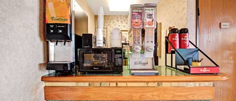 A hotel reception area with a coffee machine, microwave, and various beverage dispensers.