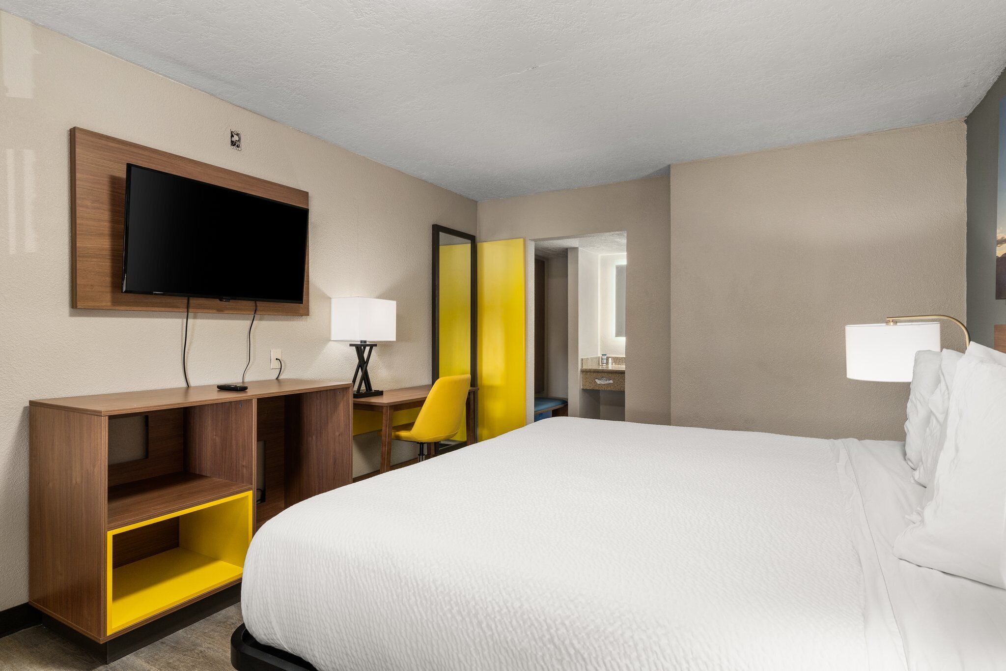 Une chambre d’hôtel avec un grand lit, un bureau avec une chaise, un téléviseur fixé au mur et un miroir.
