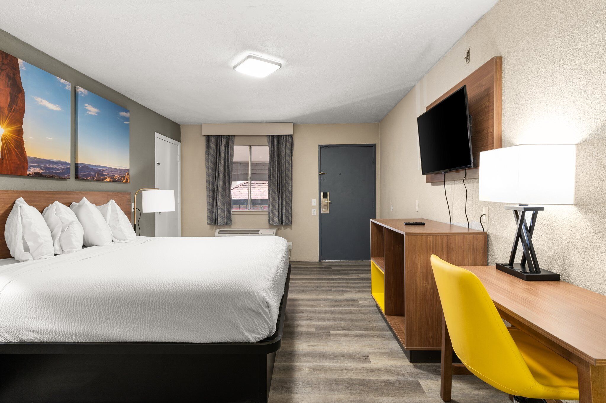 A hotel room with a bed, a desk with a chair, a TV, and a window with curtains.